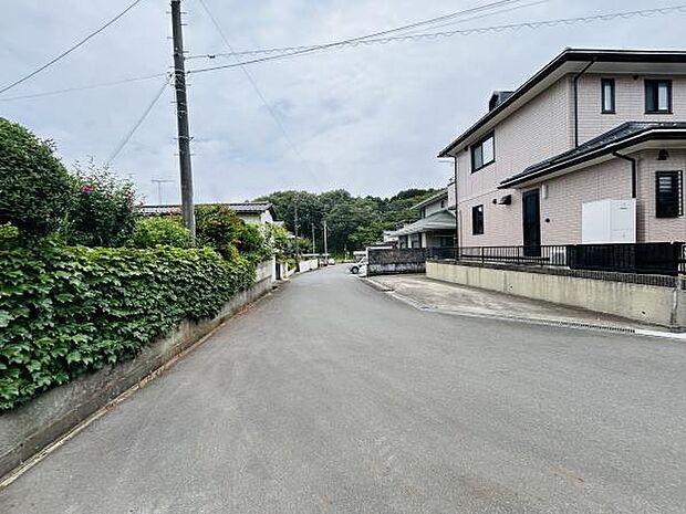 現地前面道路は幅が広く車の通行や歩行がしやすい環境です。周辺は落ち着いた住宅街で緑も多く感じられます。舗装状態も良好で快適に利用できる道路です。隣接する住宅も整然としており安心感があります。