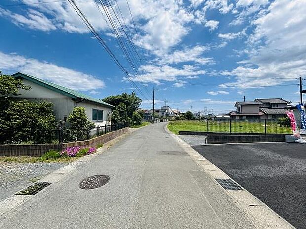 前面道路はゆとりある幅で車の出入りも安心できる環境です。周囲には住宅や緑が広がり落ち着いた雰囲気が伝わります。空の広がりを感じることができる開放的な現地です。