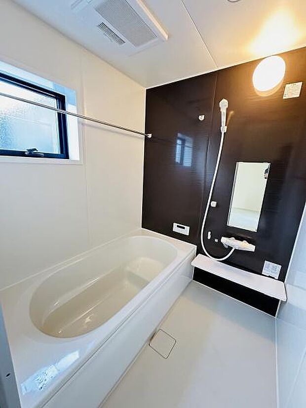 清潔感のあるバスルームで明るい空間が広がっています。便利な窓付きで換気もスムーズです。壁面のブラックパネルが全体を引き締めシンプルなデザインが魅力です。使い勝手の良い水栓や手すりも設置されています。