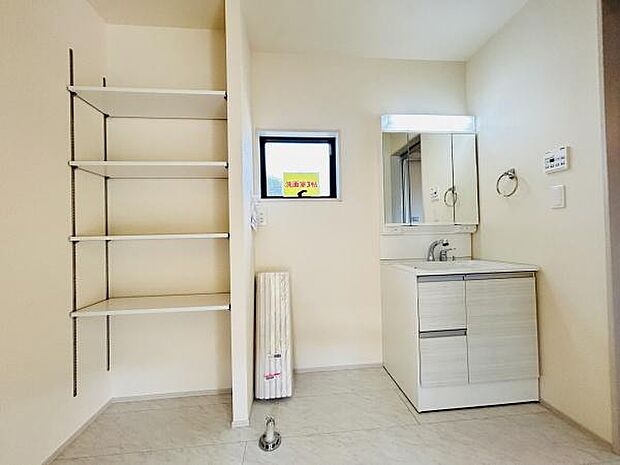 洗面所には壁付けの収納棚があり整理整頓がしやすい仕様です。コンパクトな洗面台が設置され空間がすっきりとしています。窓があるため換気にも配慮されています。室内のシンプルな色合いが印象的です。