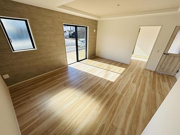 明るい光が差し込むリビングが印象的です。木目調フローリングが空間に温かみを与えています。壁面の質感がシンプルな中にもアクセントになっています。掃き出し窓もあり開放感を感じられる一室です。