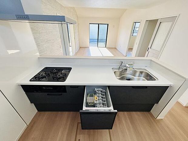 黒を基調としたキッチンはスタイリッシュな印象です。食洗機と三口コンロが備わっており調理や片付けがしやすい設計です。シンクも広く使いやすい配置となっています。リビングダイニングとの一体感も感じられます。