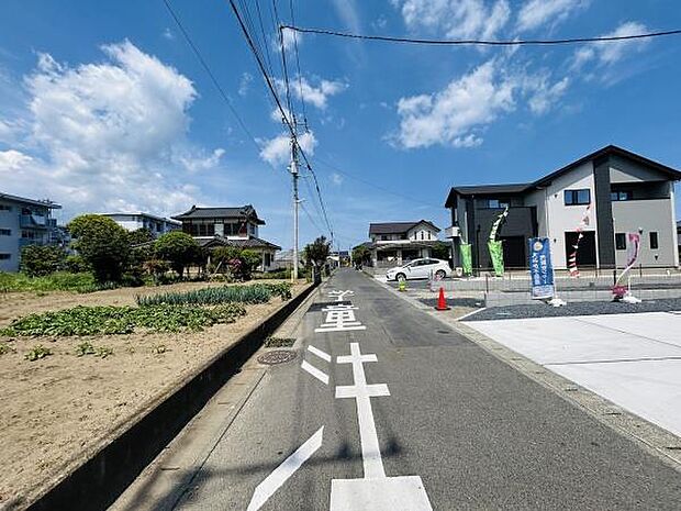 前面道路が広く車の出し入れがしやすい環境です。電柱や標識も整備され周囲は落ち着いた住宅街です。道路沿いには新しい住宅が並び開放感があります。青空が広がり開けた印象の現地です。