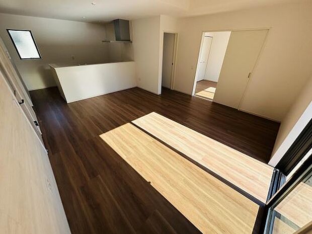 リビングは大きな窓からたっぷりと自然光が入り明るい空間が広がっています。ダークトーンの床が落ち着いた印象を与えます。キッチンとの一体感がありすっきりとしたデザインです。