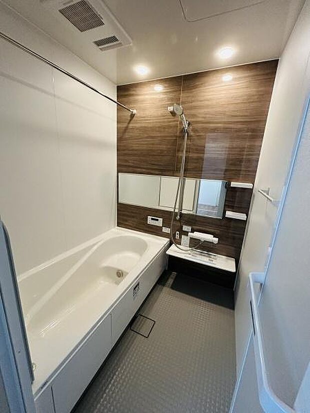 木目調のパネルがアクセントとなった落ち着きのある空間です。浴槽と洗い場が広々としており使いやすい設計です。天井に換気扇が設置されており湿気対策も施されています。照明が明るく清潔感のあるバスルームです。