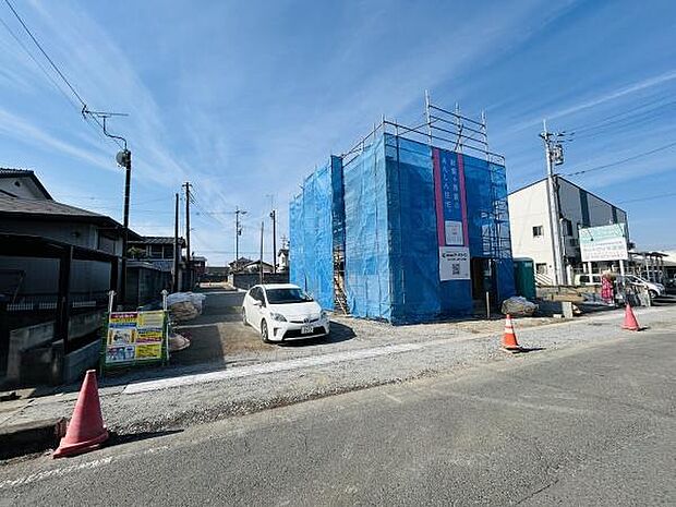 建築中の建物が青いシートでしっかりと覆われており工事の進捗が一目で確認できます。道路に面した立地で車の出入りもスムーズです。周囲は開けており明るい雰囲気が感じられます。