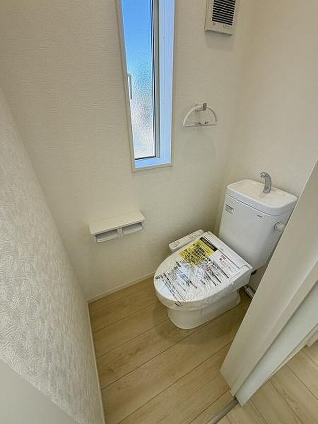 窓付きで明るさを感じられるトイレです。スペースにゆとりがあり清潔感のある仕上がりになっています。ペーパーホルダーや換気設備も設置されています。床材の色合いも落ち着いています。