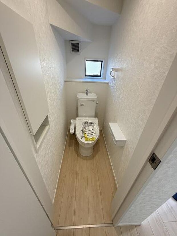 明るい雰囲気のトイレです。温水洗浄便座が設置されています。小窓があり自然光が入ります。壁紙や床材がシンプルで清潔感があります。コンパクトながらも使いやすい配置です。
