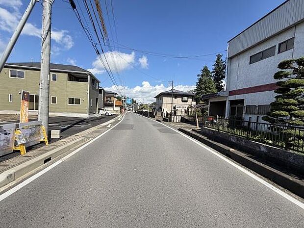 前面道路は幅があり見通しの良い環境が広がっています。道路沿いには住宅や施設が並び落ち着いた街並みが感じられます。青空が広がっており日当たりも期待できます。