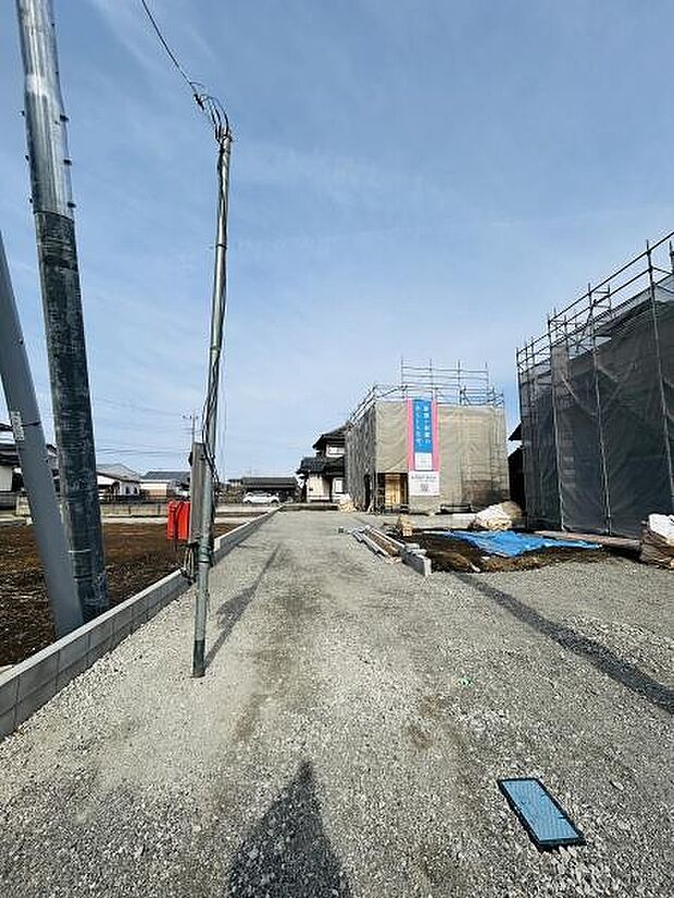 幅広い通路が確保されており車両の出入りもスムーズに行えます。周囲は整然とした住宅地で建築中の物件も並んでいます。敷地内のインフラ設備も確認できます。明るい日差しが差し込む環境です。