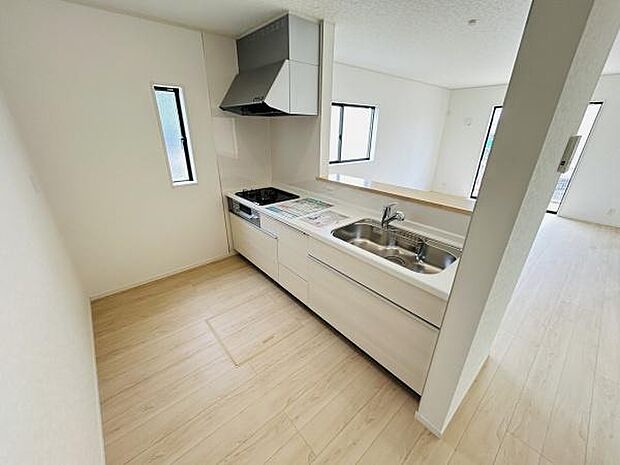 明るい色合いの木目調フローリングが特徴的なキッチンです。シンプルなシンクやガスコンロが配置され作業スペースもゆとりがあります。窓から光が差し込み開放感のある雰囲気です。