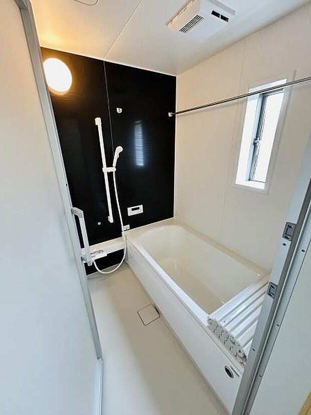 浴室は明るい色合いとダークカラーのアクセントパネルが調和しています。換気や採光に優れた窓付きです。手すりも設置され安全面にも配慮されています。ユニットバス仕様でお手入れしやすいです。