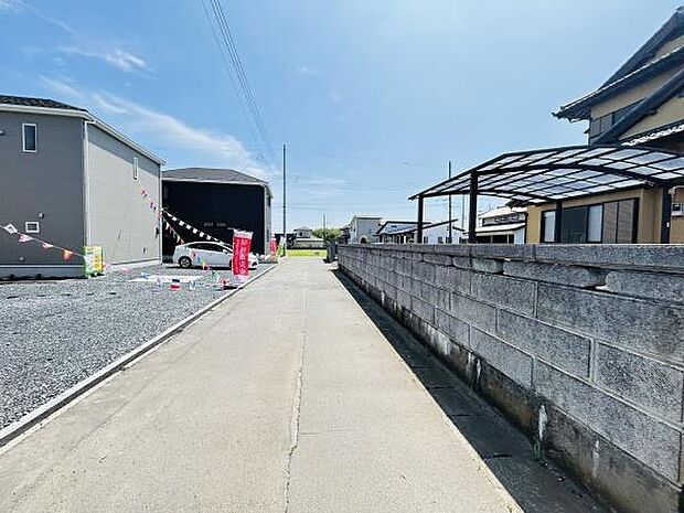 前面道路は広々とした印象で車や歩行者の通行も安心です。晴天の下周囲の住宅も整っており明るい景観が魅力です。道路沿いの塀や建物も丁寧に管理されています。周辺は落ち着いた雰囲気が感じられます。