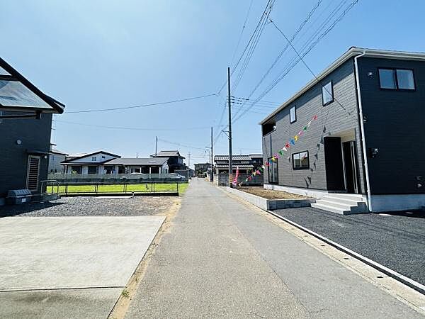 前面道路は幅が広く車の出入りがしやすい環境です。周囲は整然とした住宅が並び落ち着いた雰囲気が感じられます。視界が開けており全体的に明るい印象を与える現地写真です。