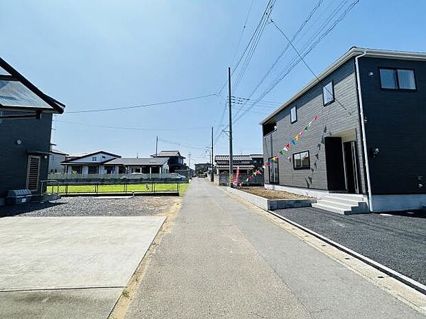 前面道路は幅が広く車の出入りがしやすい環境です。周囲は整然とした住宅が並び落ち着いた雰囲気が感じられます。視界が開けており全体的に明るい印象を与える現地写真です。