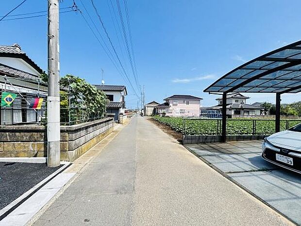 前面道路は広々としており車の出入りがしやすい印象です。周囲には住宅や畑があり落ち着いた雰囲気を感じられます。道路沿いには電柱や駐車スペースも整備されています。天気の良い日には青空がよく映えます。