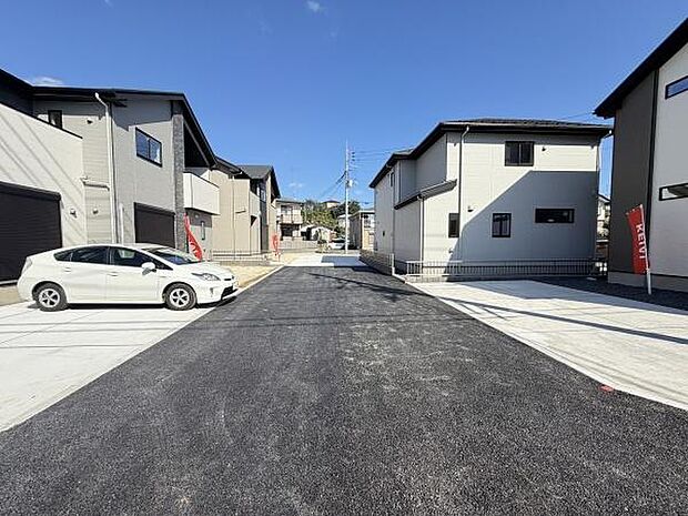 前面道路が広く整備されており車の出入りがしやすい現地写真です。両側の住宅が整然と並び統一感のある街並みが広がっています。日当たりもしっかり確保され明るい印象です。