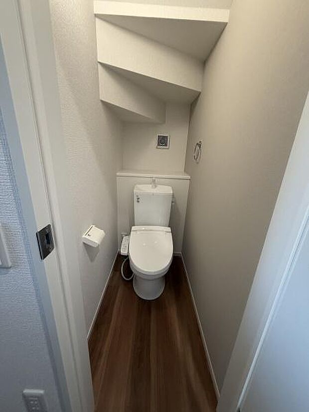限られたスペースを有効活用したトイレで収納や掃除がしやすい設計です。白を基調とした内装で清潔感があります。床の木目調が空間に落ち着いた雰囲気を与えています。