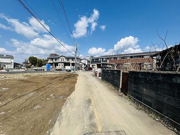 現地写真からは周囲に住宅が立ち並び静かな環境が感じられます。前面道路は車両の通行に十分な幅員が確保されています。空が広く日当たりが期待できる雰囲気です。