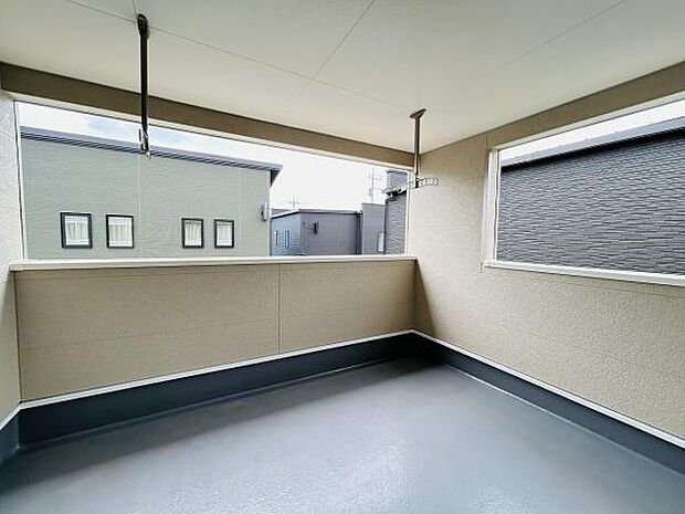 屋根付きで天候に左右されにくいバルコニーです。壁が高めなのでプライバシーを確保できます。広々とした空間が確保されており使い勝手の良さが特徴です。手すり部分や物干し用の金具も設置されています。