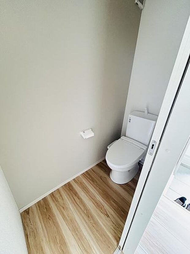 シンプルな内装が特徴のトイレです。床材には木目調が使用されています。壁面も明るい色でまとめられ清潔感があります。ペーパーホルダーも壁付けで空間がすっきりしています。