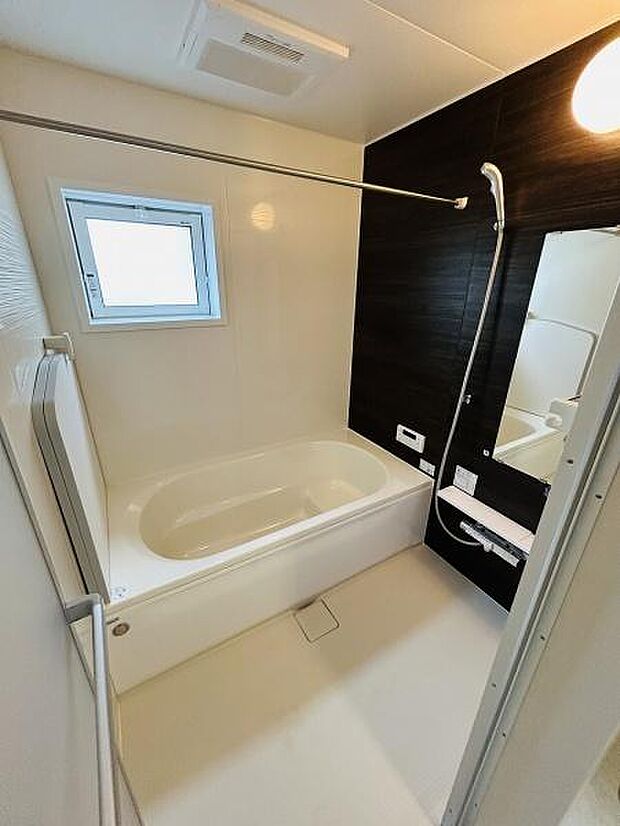 窓付きで換気しやすいバスルームです。シンプルなデザインでお手入れしやすくなっています。浴槽とシャワーが別で使いやすい仕様です。壁面のアクセントカラーが空間を引き締めています。