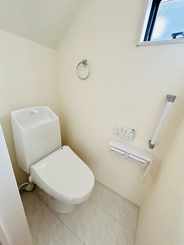 明るい壁と窓からの採光が特徴のトイレです。手すりや操作パネルも設置されており利便性に配慮されています。ペーパーホルダーやタオルリングも揃った清潔感のある空間です。
