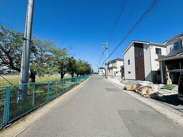 前面道路は見通しが良く開放感のある直線道路が続いています。周囲には住宅と緑が調和しており落ち着いた雰囲気です。青空が広がる環境も印象的な現地写真となっています。周辺はすっきりとした街並みです。