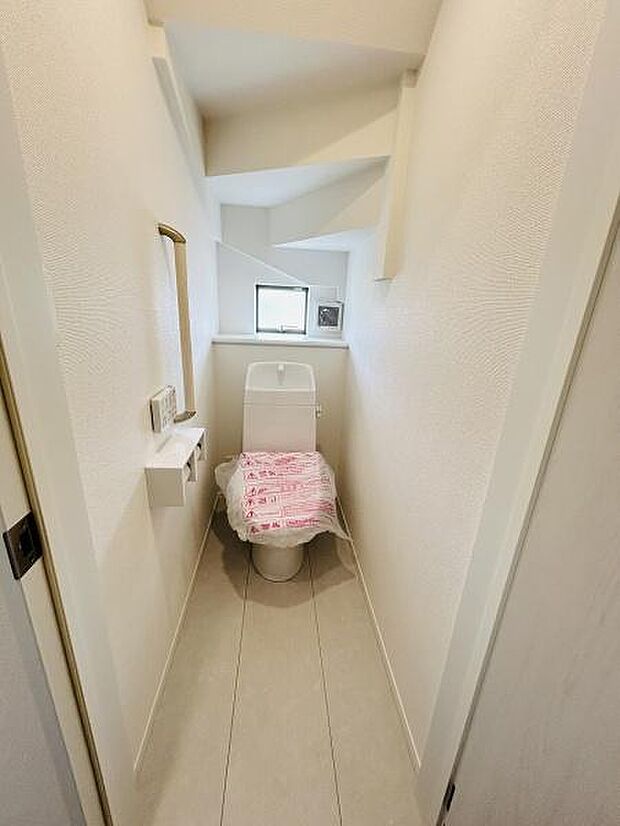 明るい色調の内装で空間がすっきりとした印象のトイレです。壁に設けられた小窓があり自然光を取り入れることができます。奥行きのある形状で清潔感があります。収納や手洗いスペースも配置されています。