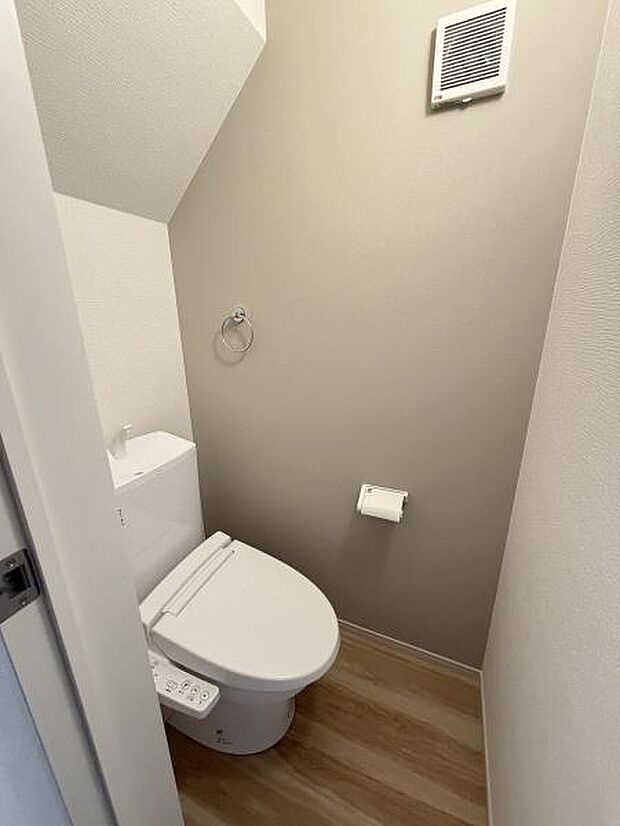 シンプルで明るいトイレ空間です。木目調の床が落ち着いた雰囲気を演出します。換気設備も設置されており快適にご利用いただけます。ペーパーホルダーやタオルリングも設置されていて便利です。