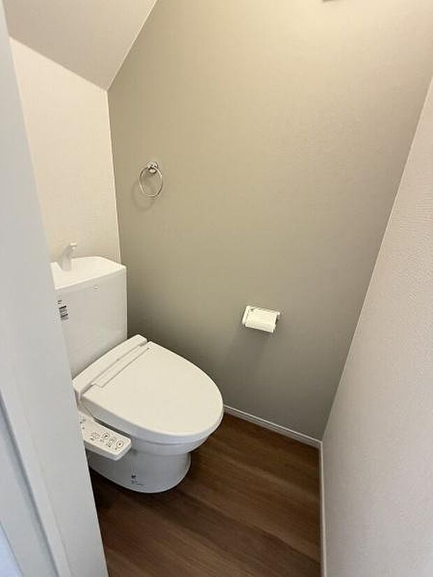 落ち着きのある色合いの壁と床が特徴のトイレです。温水洗浄便座が設置されています。ペーパーホルダーやタオルリングなどの設備も充実しています。スペースにゆとりがあり使い勝手が考えられています。