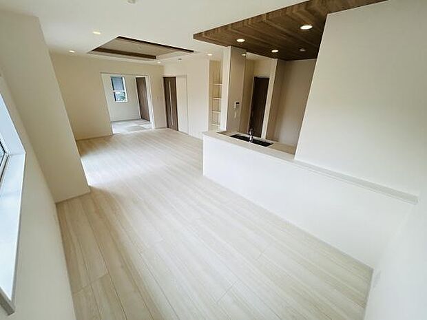 明るい色合いの床材が空間全体を軽やかに演出しています。天井のデザインがアクセントとなり雰囲気に変化をもたらしています。リビングとキッチンのつながりがスムーズで開放感ある空間構成です。
