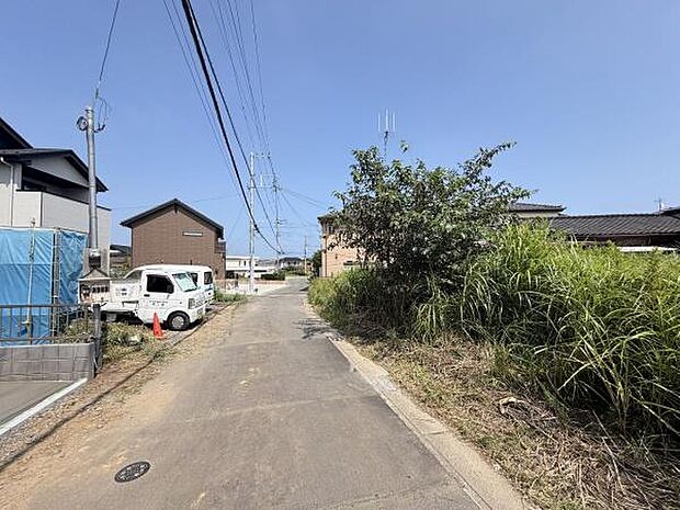 前面道路はゆったりとした幅員で車の出入りがしやすい環境です。周辺には住宅が建ち並び落ち着いた雰囲気が感じられます。道路沿いの植栽も整備されており現地の様子がしっかり確認できます。