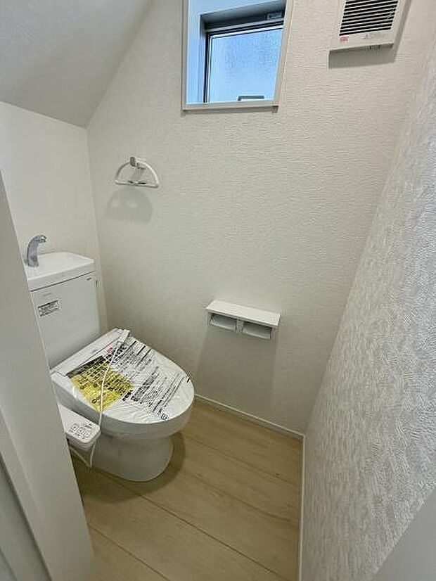 シンプルなデザインのトイレです。窓があり明るい空間となっています。壁面の質感や床材も統一感があります。ペーパーホルダーや換気扇も備わっています。使い勝手を考慮したレイアウトです。