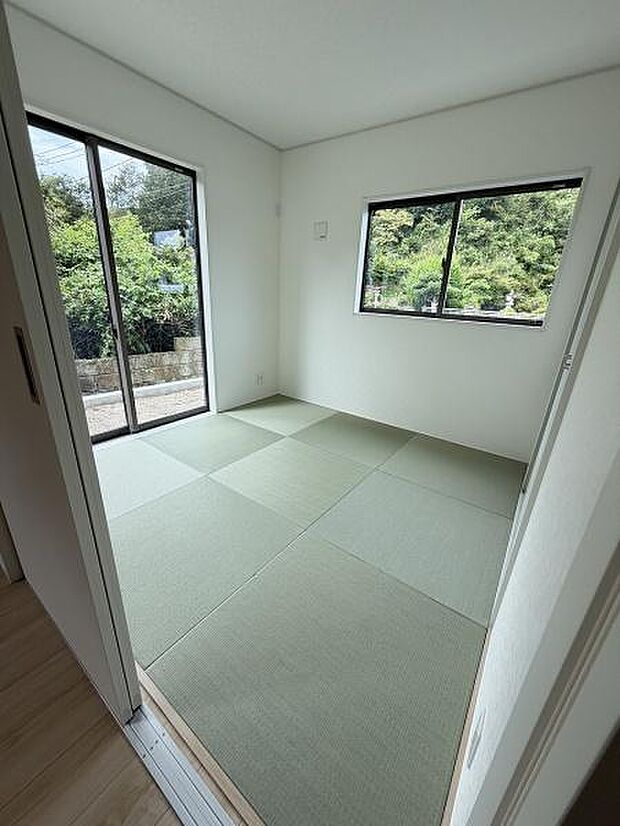 大きな窓から自然光が差し込む和室です。シンプルな内装でお手入れもしやすい空間となっています。畳の落ち着いた色合いが特徴的です。窓から緑も楽しめる環境です。