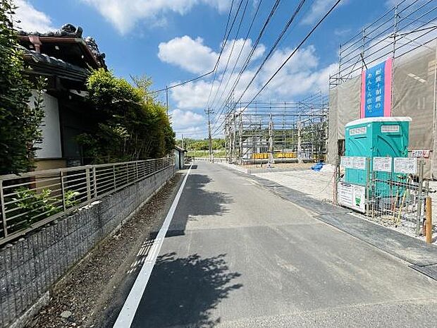 前面道路は幅員があり車の通行もしやすい環境です。舗装された道路が続き現地までスムーズにアクセスできます。電線や建築中の建物が並び周囲は開放感のある雰囲気です。天候も良く明るい印象を受ける現地写真です。
