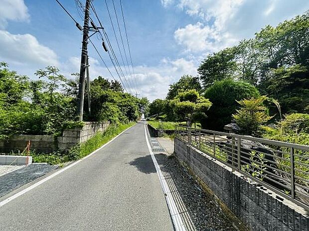 前面道路は舗装されており綺麗に整備されています。周囲には緑が多く自然に囲まれた環境です。電柱やフェンスも設置されており安心感を感じられます。開放感のある道路沿いで見通しの良い立地です。