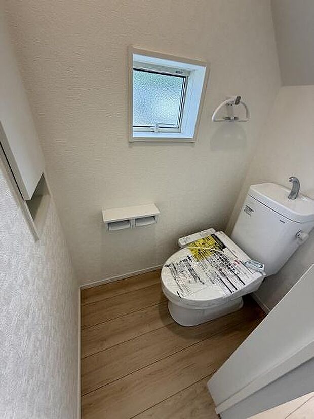 コンパクトな空間に設計されたトイレです。採光を取り入れる窓があり明るさが感じられます。シンプルな内装で清潔感があります。床と壁のカラーも調和しています。紙巻器や収納など必要な設備が備わっています。