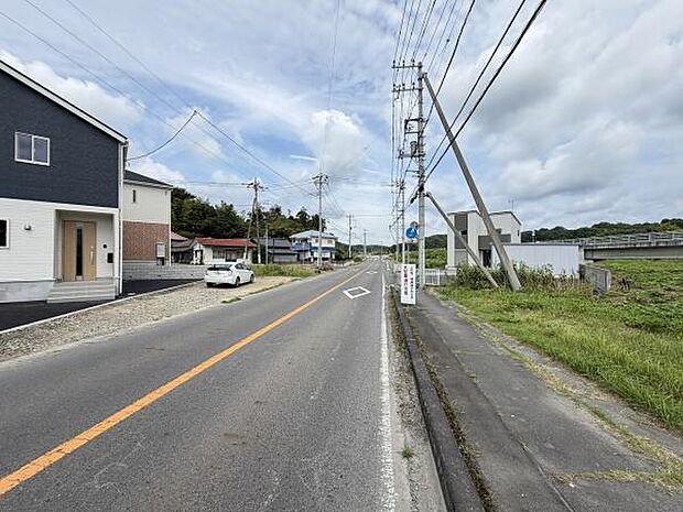 前面道路は幅員が広く車の出入りがしやすい環境です。周辺には緑も多く開放感があります。電柱や舗装もしっかりしており日常の移動に便利です。現地の様子がよく分かる写真です。