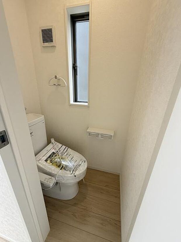 シンプルで清潔感のあるトイレです。窓があり自然光が差し込む明るい空間となっています。壁面の換気口も設置されており快適な環境が保たれます。床材との調和も良く落ち着いた雰囲気を演出しています。