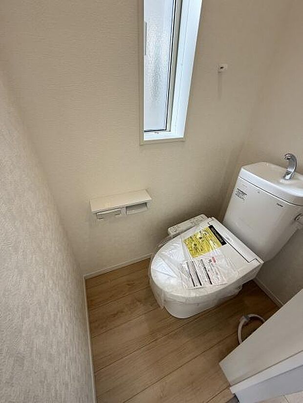 清潔感のあるシンプルなトイレ空間です。明るい内装とやわらかな木目調の床が空間をすっきりと見せています。小窓が設けられており換気や採光に配慮されています。