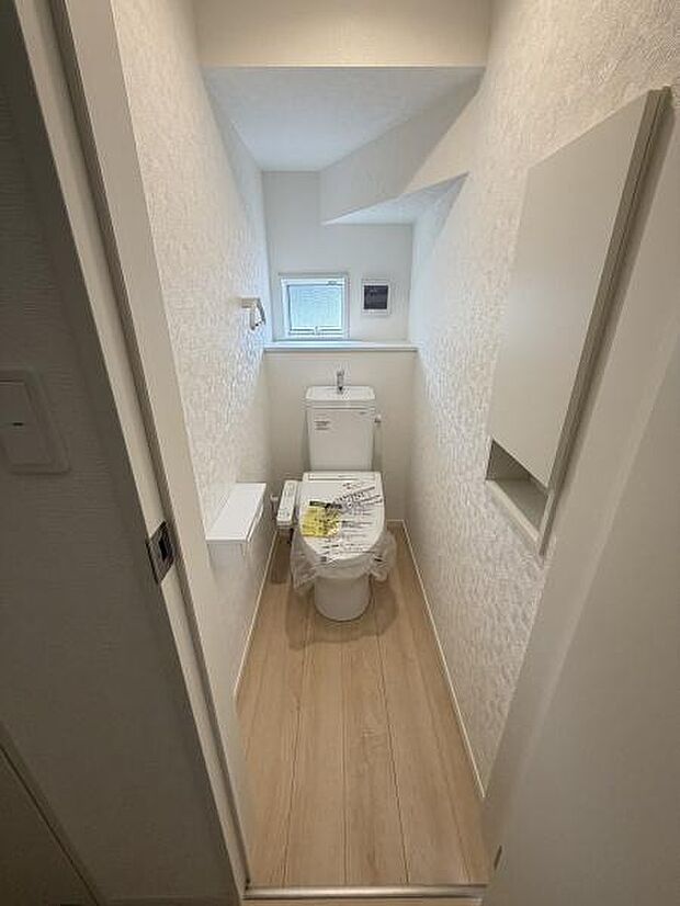明るい色調の内装が特徴的なトイレです。小窓が設けられており自然光を取り入れやすい設計となっています。壁面収納も備えられており空間がすっきりとしています。床材の色合いが全体の雰囲気を引き締めています。