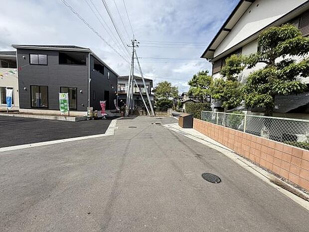 ゆったりとした幅の前面道路が特徴の現地写真です。周辺には住宅が建ち並び落ち着いた雰囲気が感じられます。すっきりと整った舗装道路が印象的です。