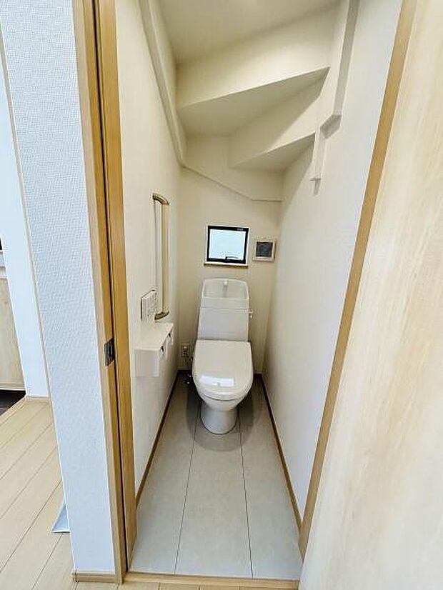 コンパクトな空間に配置されたトイレです。小窓があり換気や明るさを確保できます。シンプルな内装で清潔感があります。ペーパーホルダー等の備品も揃っています。壁や床材も淡い色合いで統一されています。