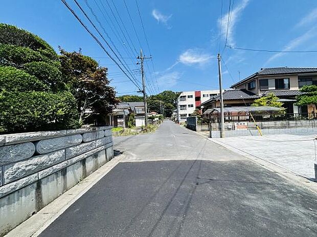 広々とした前面道路が印象的な現地写真です。アスファルト舗装がきれいで周辺には緑豊かな植栽が見られます。道路沿いには住宅が整然と並び落ち着いた雰囲気が特徴です。