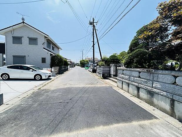 前面道路は舗装され車の通行もスムーズにできる環境です。周囲には住宅が立ち並び落ち着いた雰囲気が広がっています。広々とした道路で車の出し入れも安心です。電柱やフェンスが整然と配置されています。