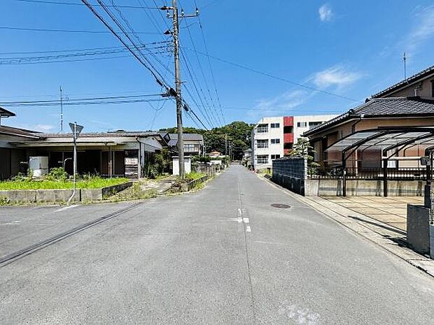 広々とした前面道路が印象的な現地写真です。車の出入りも安心できるゆとりある道幅です。周辺には住宅が建ち並び落ち着いた雰囲気が感じられます。青空が広がり陽当たりの良さも魅力です。