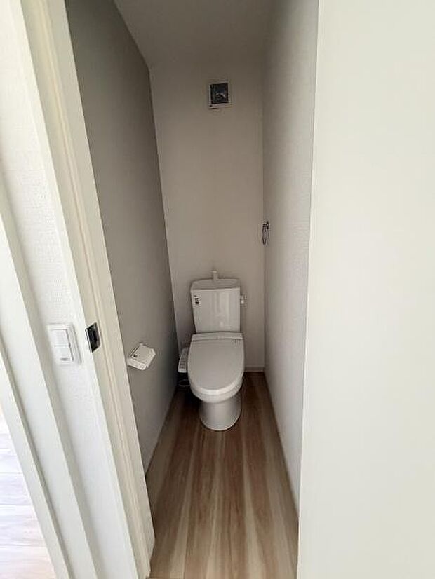 シンプルなデザインで使いやすいトイレです。換気設備が設置されており清潔感のある空間となっています。床はナチュラルな色合いで落ち着いた印象です。ペーパーホルダーの位置も使いやすい配置です。
