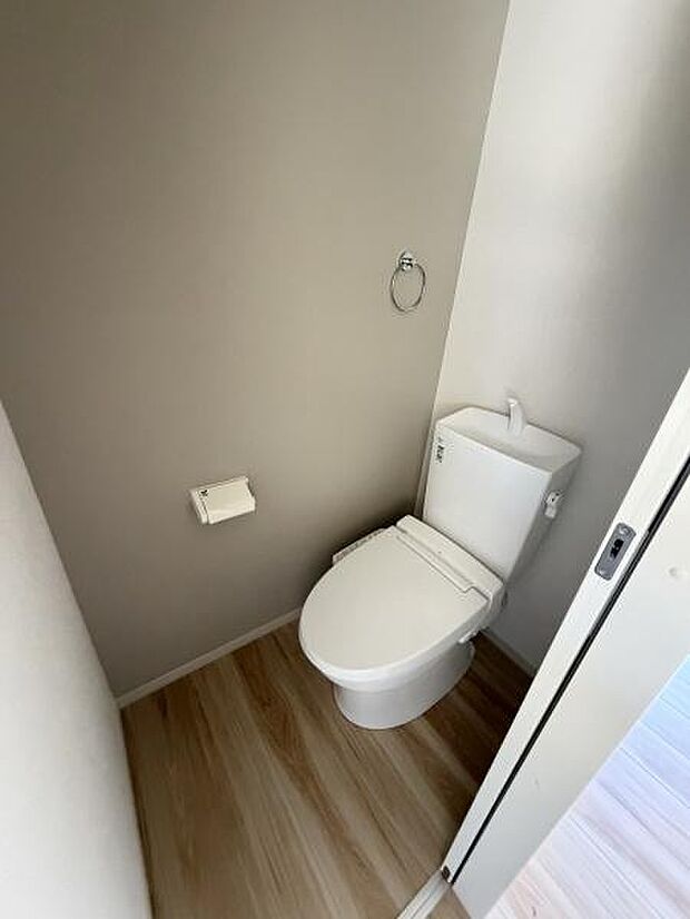 落ち着いた色合いの内装が特徴のトイレです。扉を開けた瞬間に清潔感が伝わってきます。ナチュラルな木目調の床が空間に調和しています。手洗い付きのデザインで使いやすさも考慮されています。