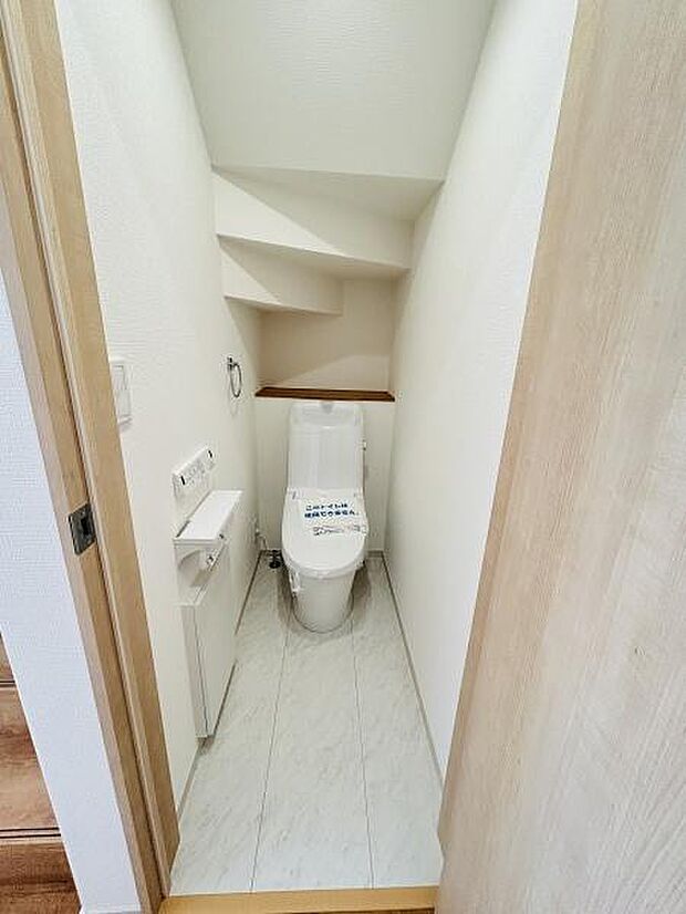 シンプルな内装で清潔感のあるトイレ空間です。コンパクトながらも収納スペースがありすっきりとした印象です。壁面のデザインにも工夫が見られます。白を基調とした床材が明るさを感じさせます。